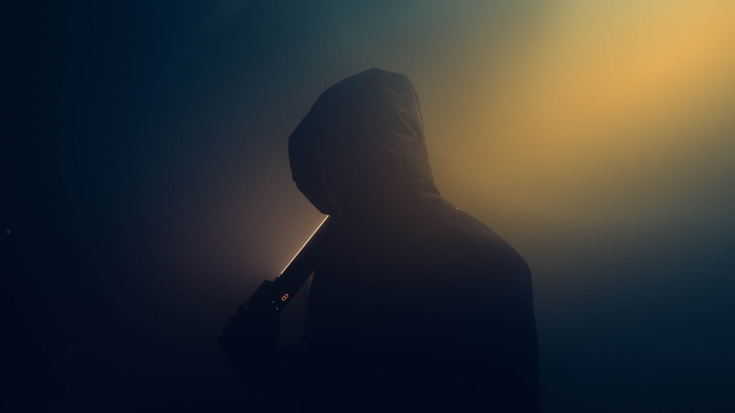 Person in a hood holding a baseball bat against a dark background with a light source creating a silhouette effect.