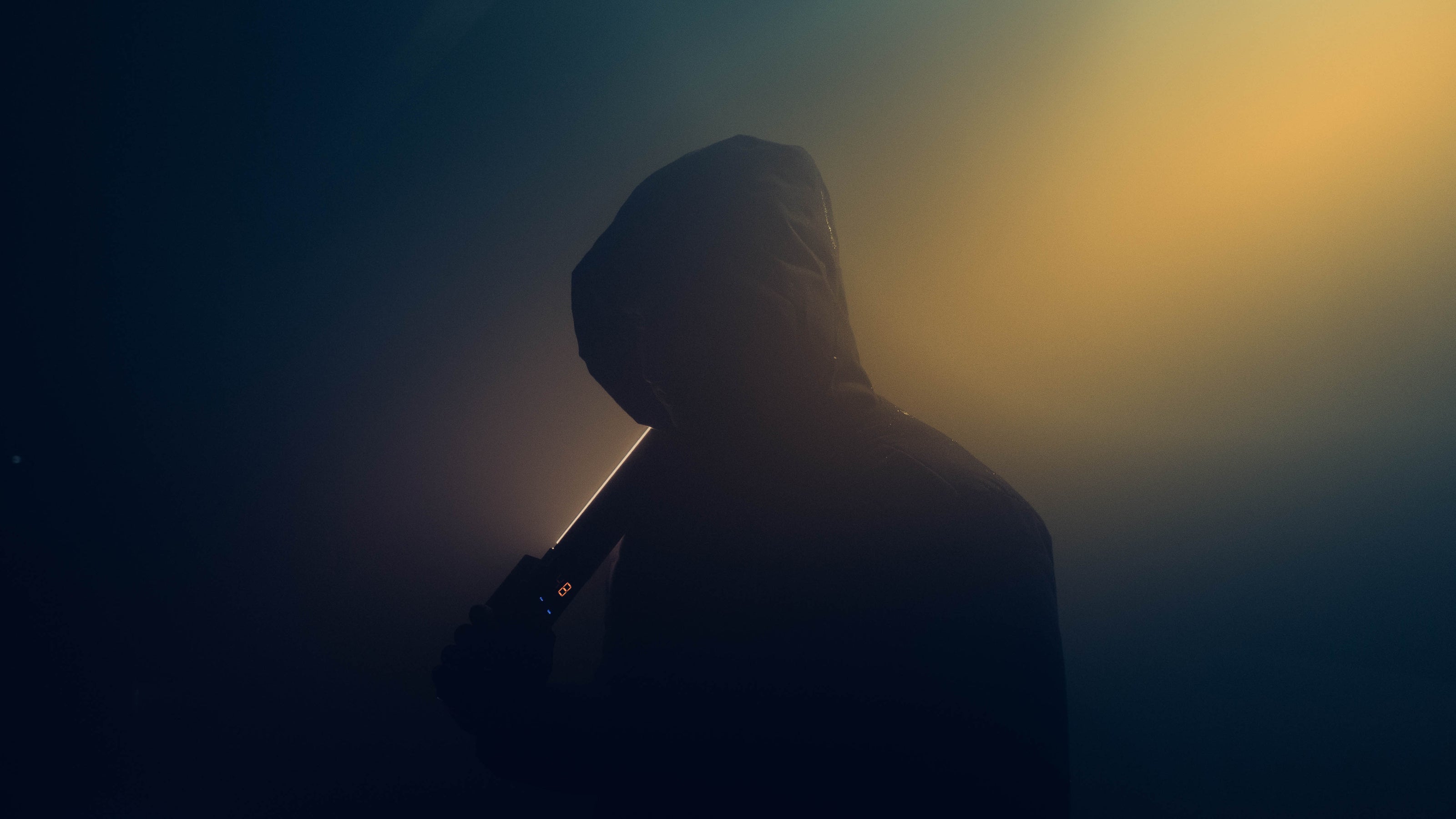 Person in a hood holding a baseball bat against a dark background with a light source creating a silhouette effect.